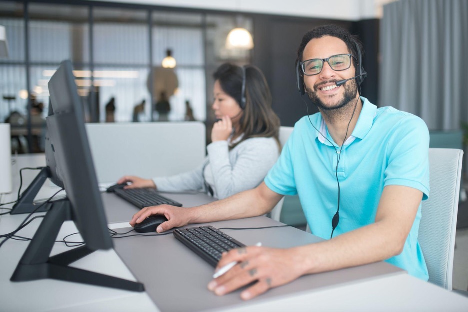 A customer support agent with a headset smiles while working on a computer.